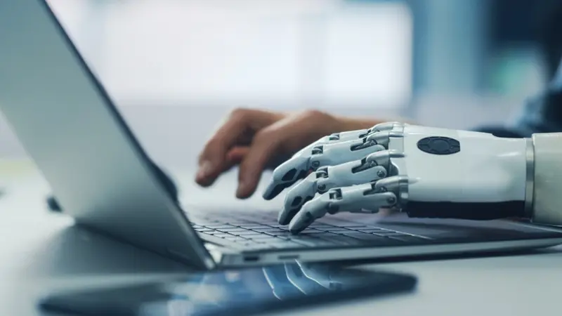 human hand and robot hand work together on a laptop